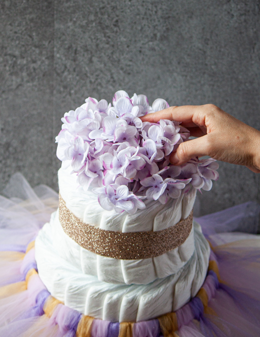 pink hydrangea floral, being placed on top of a diaper cake with gold ribbon and pink, purple and gold tutu. 
