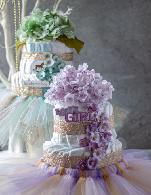 pink, purpler and gold decorated girls diaper cake  and a green , blue and gold decorated  boys diaper cake in the background. 
