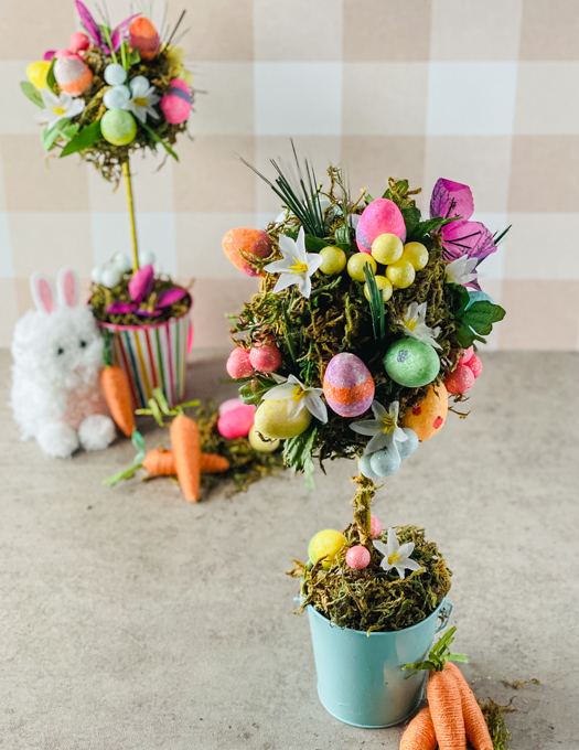 two topiary trees fully decorated with eggs, flowers and greenery, with carrots and white bunny