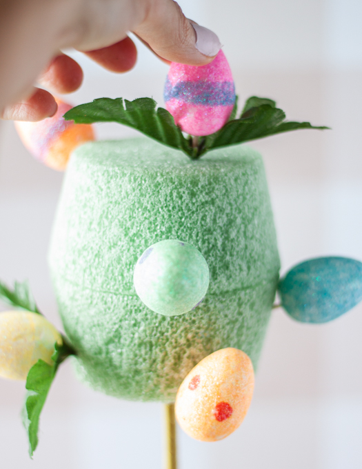 colorful foam eggs with green leaves attached in a green pot insert and pink egg being attached in top