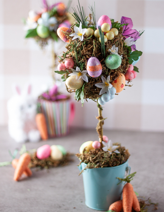 topiary tree in a blue bucket decorated with colourful eggs, flowers, grass and moss