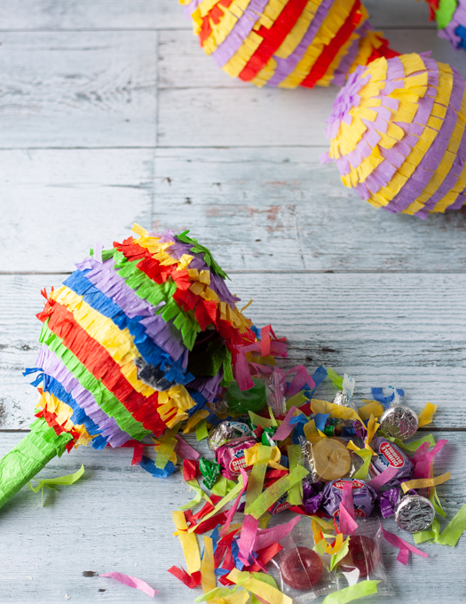 smashed colourful mini pinata with candy and confetti on the table and other piniatas on top