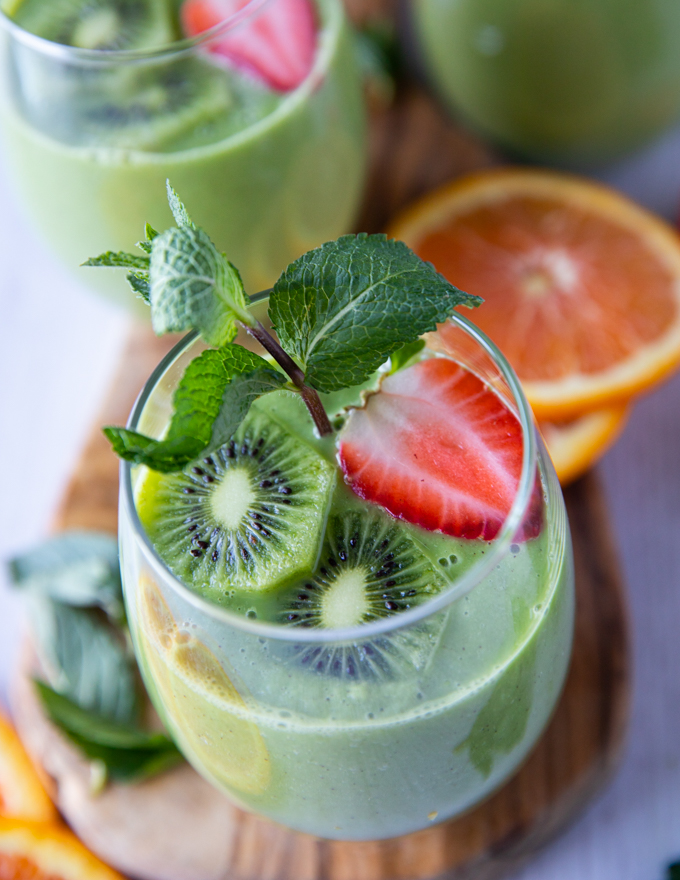 A Cup of Spinach Smoothie garnished with mint, kiwi, and strawberry slices